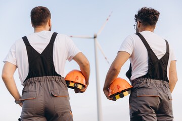 Engineers holding helmets looking at wind turbine in the desert