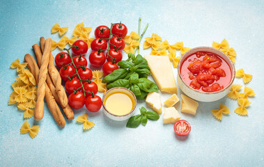 Ingredients for cooking Italian dish. Tomato sauce, grissini, farfalle pasta, spaghetti, fresh tomatoes, basil, parmesan cheese, and olive oil on blue background