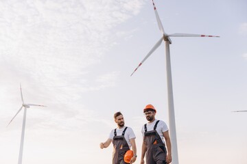 Arabian engineers walking and discussing near wind turbines in a field