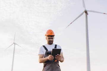 Technician working with digital tablet next to wind turbines for renewable energy