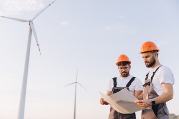 Engineers examining blueprints at wind turbine farm for sustainable energy production