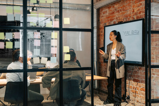 Businesswoman conducting meeting with male and female colleagues sitting in board room