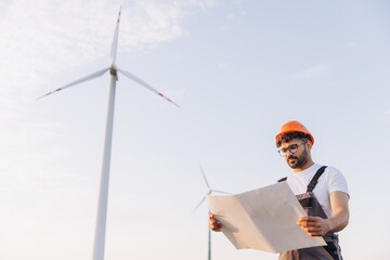 Engineer reading blueprints on a wind turbine farm for renewable energy