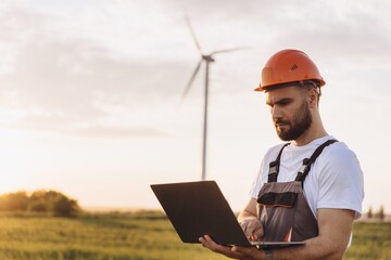 Engineer working on a laptop in a wind turbine power plant at sunset