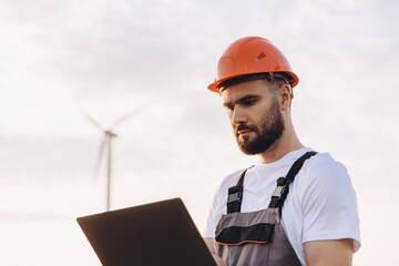 Engineer working on a laptop with a wind turbine in the background