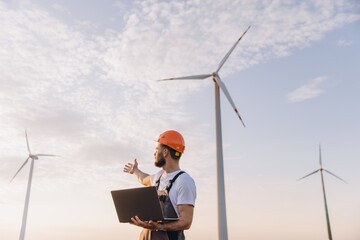 Engineer holding laptop inspecting wind turbines in a wind farm