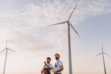 Engineers inspecting wind turbines in a wind farm at sunset