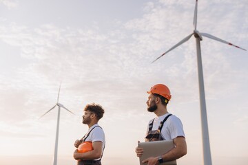 Engineers inspecting wind turbines in a wind farm at sunset