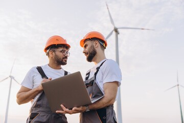 Engineers discussing holding laptop in wind turbine farm
