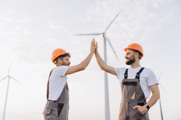 Arabian engineers giving high five celebrating sustainable energy in wind turbine power plant