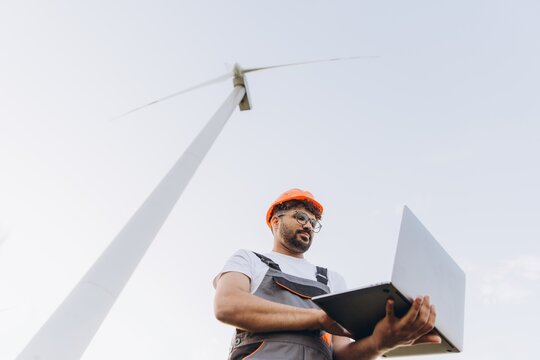 Arabian engineer working on a laptop next to a wind turbine