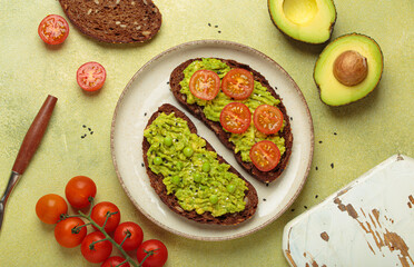 Slices of whole grain rye bread with mashed avocado, green peas and cherry tomatoes seasoned with black sesame seeds are served on a plate for a healthy breakfast or snack