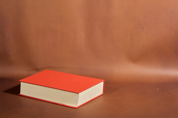 Detail of a Book with Red Cover and Cream Pages on Brown Background
