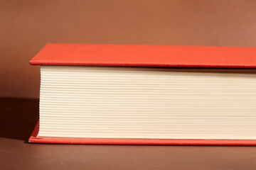 Detail of a Book with Red Cover and Cream Pages on Brown Background
