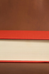 Detail of a Book with Red Cover and Cream Pages on Brown Background
