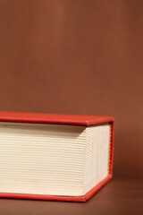 Detail of a Book with Red Cover and Cream Pages on Brown Background
