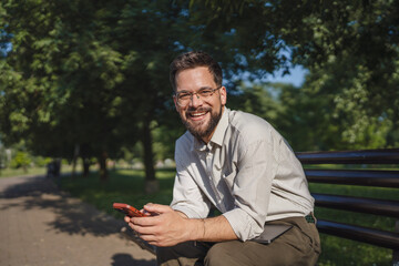Fototapeta premium Adult man sit on bench in a public use mobile phone, leisure activity