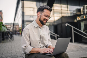 happy satisfied businessman sit on street during break and use laptop