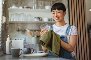 happy mature japanese woman wiping dishes at home kitchen