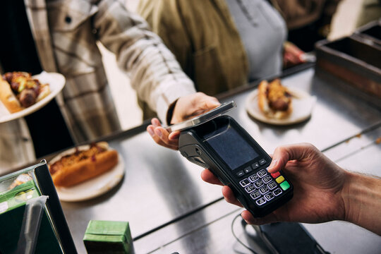 Hand of owner holding credit card reader while customer making payment through smart phone at food truck