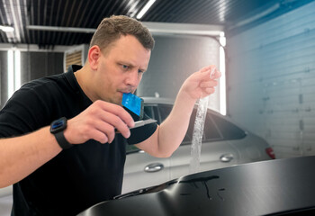 A car wrapping specialist applies a polyurethane film to the car. Detailer smoothes PPF. Car wrapping, detailing, tuning and styling. Selective focus. PPF protective film against chips and scratches. 