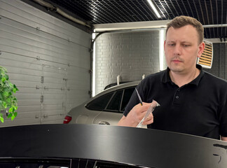 A car wrapping specialist applies a polyurethane film to the car. Detailer smoothes PPF. Car wrapping, detailing, tuning and styling. Selective focus. PPF protective film against chips and scratches. 