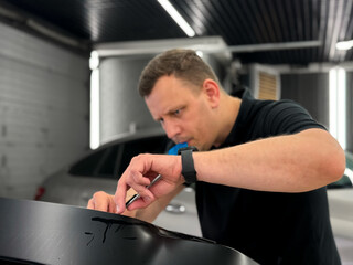 A car wrapping specialist applies a polyurethane film to the car. Detailer smoothes PPF. Car wrapping, detailing, tuning and styling. Selective focus. PPF protective film against chips and scratches. 