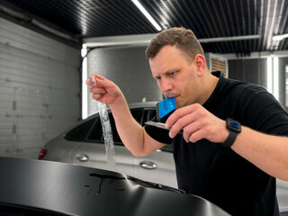 A car wrapping specialist applies a polyurethane film to the car. Detailer smoothes PPF. Car wrapping, detailing, tuning and styling. Selective focus. PPF protective film against chips and scratches. 