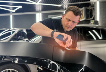 A car wrapping specialist applies a polyurethane film to the car. Detailer smoothes PPF. Car wrapping, detailing, tuning and styling. Selective focus. PPF protective film against chips and scratches. 
