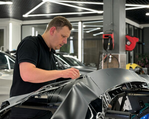 A car wrapping specialist applies a polyurethane film to the car. Detailer smoothes PPF. Car wrapping, detailing, tuning and styling. Selective focus. PPF protective film against chips and scratches. 