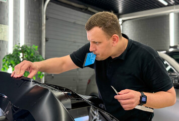 A car wrapping specialist applies a polyurethane film to the car. Detailer smoothes PPF. Car wrapping, detailing, tuning and styling. Selective focus. PPF protective film against chips and scratches. 