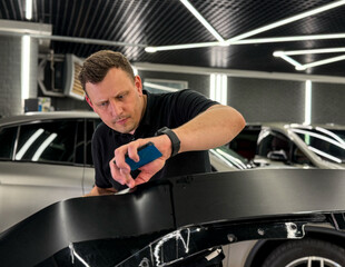 A car wrapping specialist applies a polyurethane film to the car. Detailer smoothes PPF. Car wrapping, detailing, tuning and styling. Selective focus. PPF protective film against chips and scratches. 