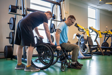 Professional sports trainer assisting hardworking disabled man in wheelchair transition from...