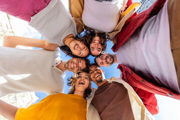 Low angle view of diverse group of young friends standing together in circle, hugging each other...