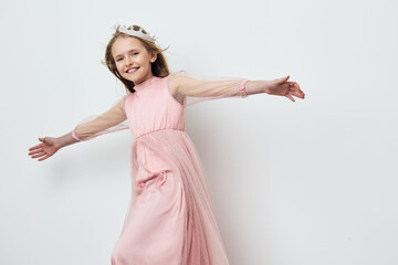 A joyful young girl in a pink dress with flowing sleeves, posing playfully against a minimalist...