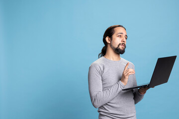 Tech savvy individual holding a laptop against a blue background, conveying calm and...