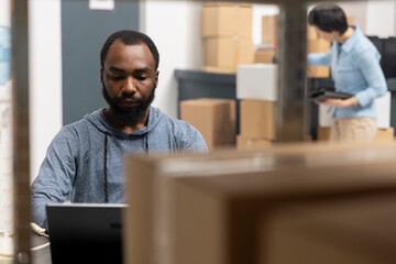 African american man overseeing product shipment and order logistics, working in small scale...