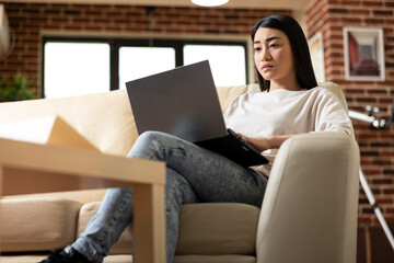 Serious female manager working remotely in brick wall apartment, typing on laptop and preparing...