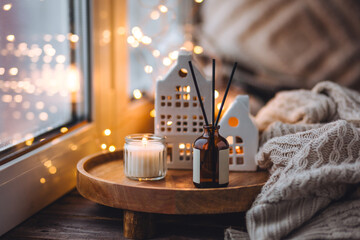 Aroma diffuser, burning candle, Christmas perfume on wooden bamboo tray, knitted sweater. Cozy home decor, hygge and aromatherapy concept. Comfortable atmosphere, Scandinavian decor.