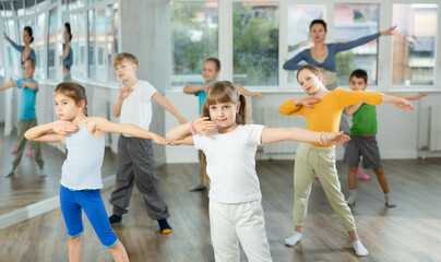 Girl learns to dance during childrens master class in studio. Teacher watches students, participates in training in background