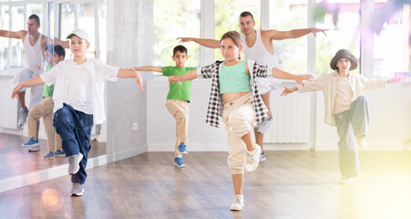 Fototapeta premium Group of young girls and boys in casualwear performing contemporary street dance in modern training room