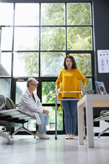 Asian woman using walking frame during rehabilitation healing process, receiving physical support...