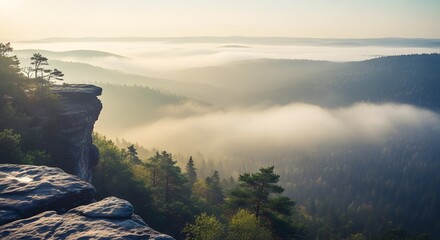 Panoramic view of a mountain range enveloped in morning mist with sunlight illuminating the landscape creating a serene atmosphere. Forested valleys and cliff faces frame the scene.