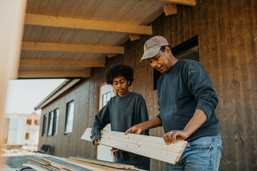 Grandson helping grandfather examining wooden plank during home renovation