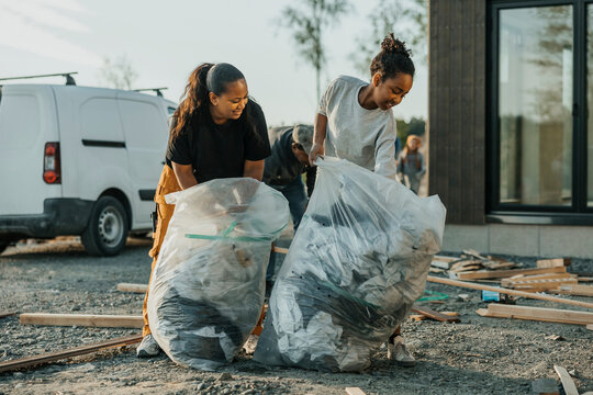 Daughter and mother collecting construction waste in trash bags outside house