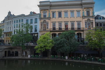 A canal in Utrecht, Netherlands, bordered by trees and historic buildings. Features a yellow...