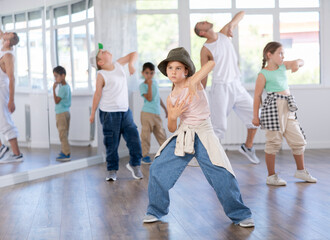 Focused preteen girl performing dynamic hip hop moves in group class for kids, led by skilled young...