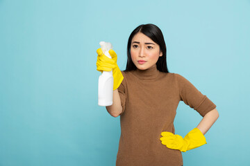 Female housekeeper confidently holding white spray bottle against isolated background. Focused...