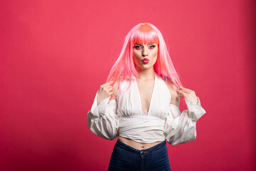 Stylish female adult in fashionable blouse and pink wig pouting confidently while holding hair....