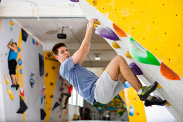 Caucasian young man looking at camera while exercising in climbing gym on wall.